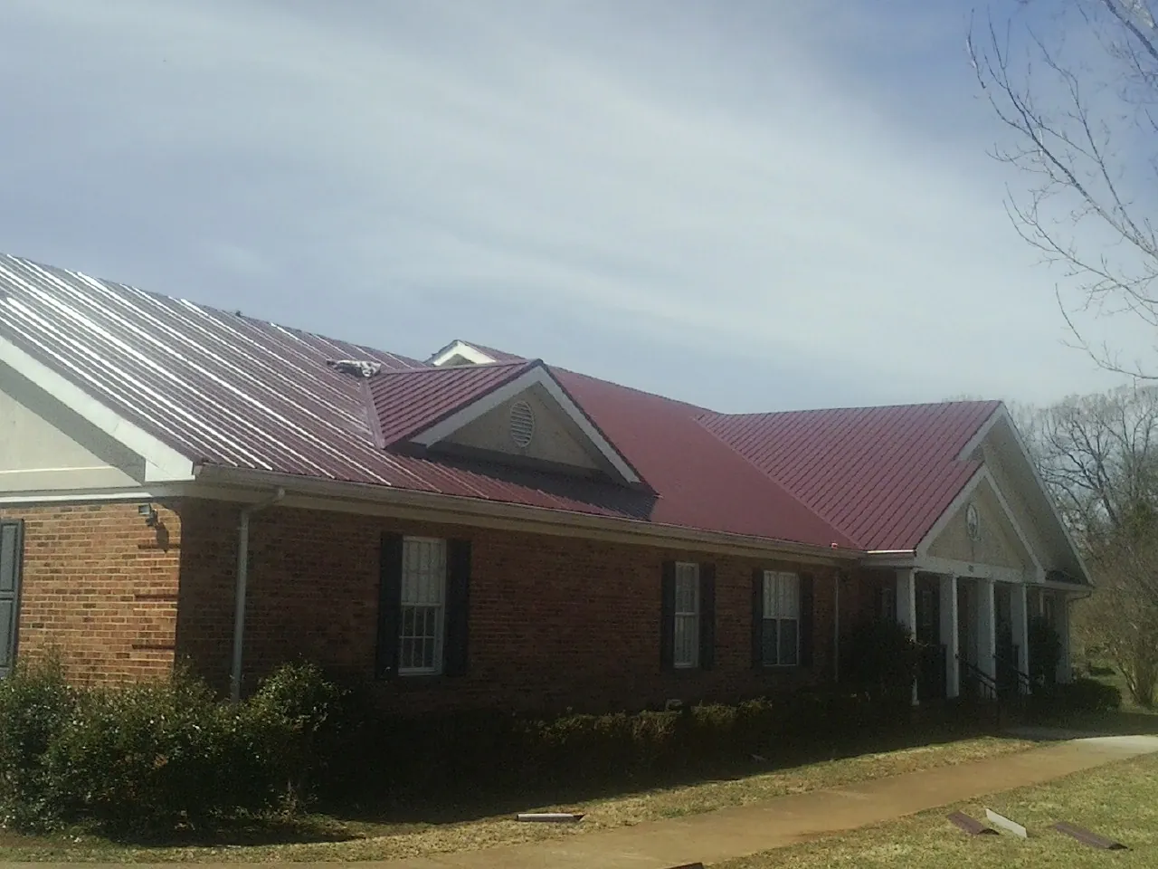 Red metal roof with gabled entries on a long brick building, from a Hail Damage Roof Repair job in Circleville