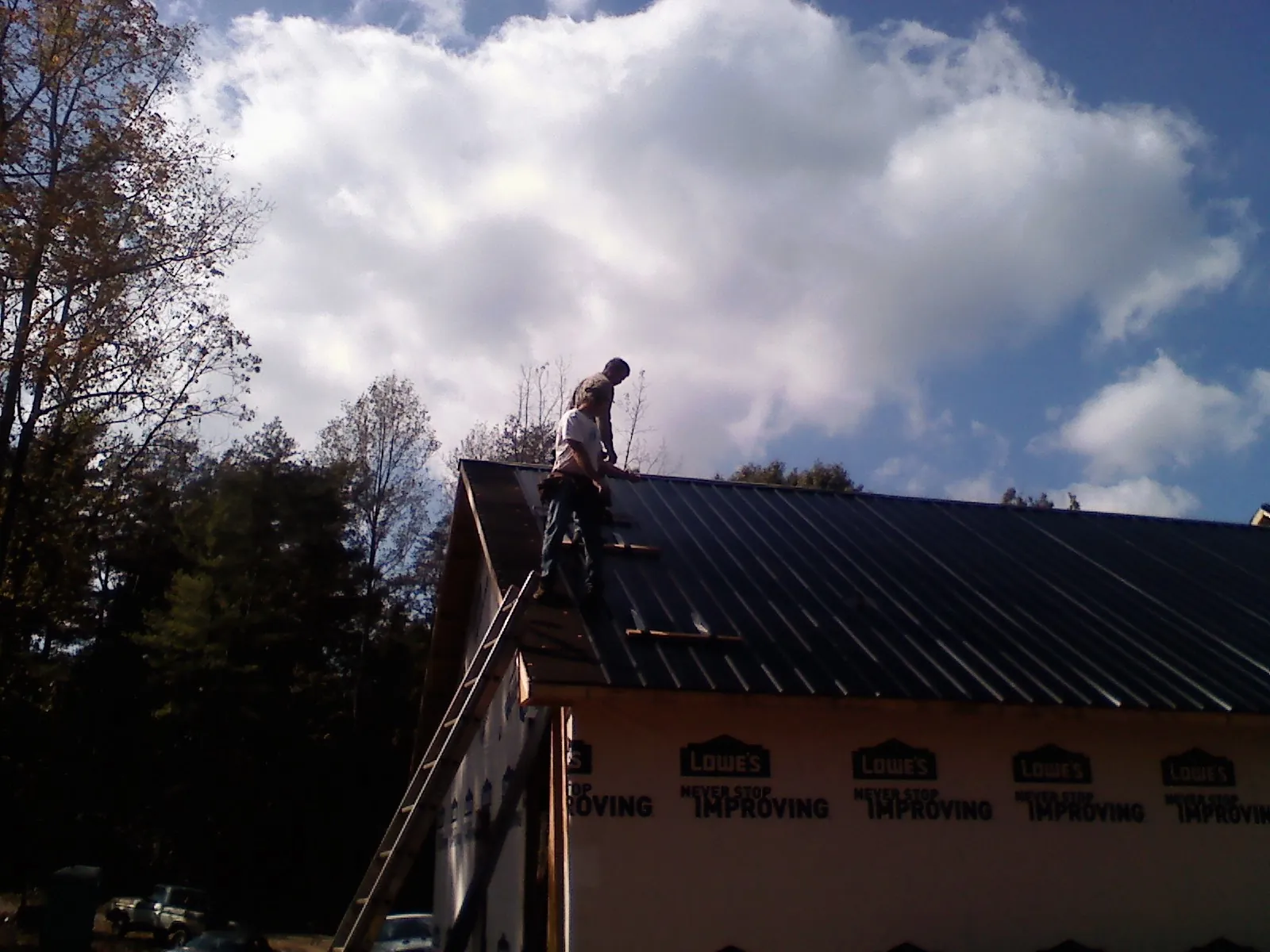 Roofer fastening dark metal panels high against a cloudy sky, from a Roof Inspection job in Circleville